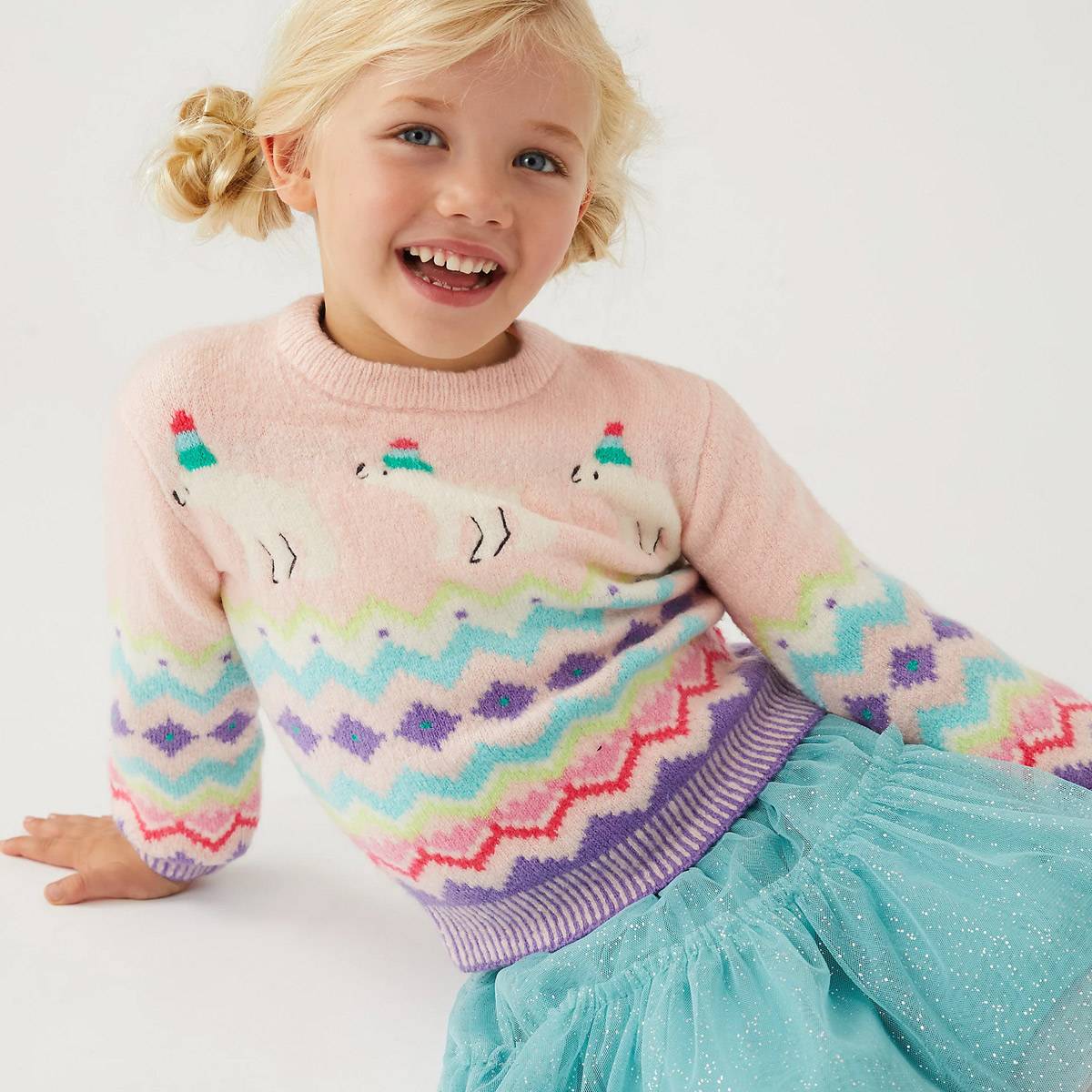Young girl wearing a pale-pink Christmas jumper. Shop girls’ jumpers